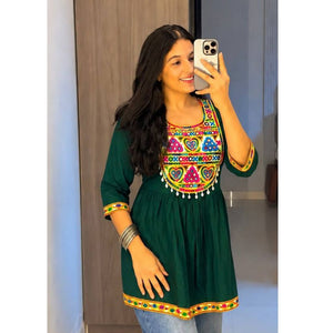 A woman taking a mirror selfie wearing a dark green cotton kurta with colorful embroidered patterns around the neckline and sleeve cuffs, paired with blue jeans.