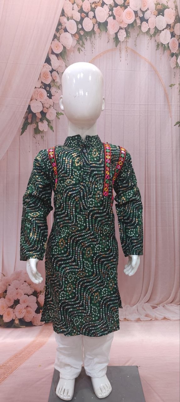 A children's long-sleeve kurta displayed on a white mannequin, featuring a dark green base with intricate gold and silver sequin patterns and red embroidered shoulder details, paired with white trousers against a pink floral backdrop.