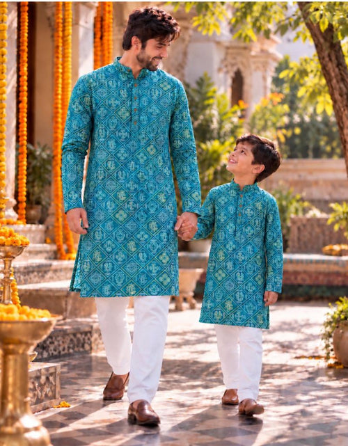 Load image into Gallery viewer, A man and a boy holding hands, wearing matching teal blue patterned kurta sets with white trousers, walking hand-in-hand in a traditional courtyard decorated with orange marigold garlands.

