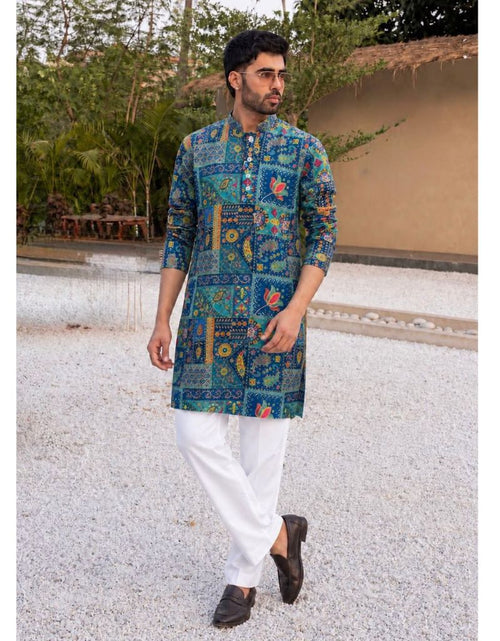 Load image into Gallery viewer, A man wearing a blue and green patterned kurta with white trousers and dark brown shoes, standing outdoors on a light gravel path with a garden and wall in the background.
