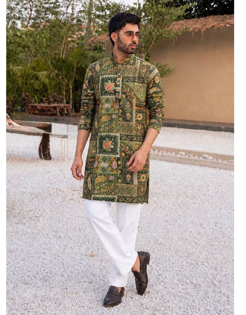 Load image into Gallery viewer, A man wearing a green and gold patterned kurta with white trousers and dark loafers, standing outdoors on a light gravel path.
