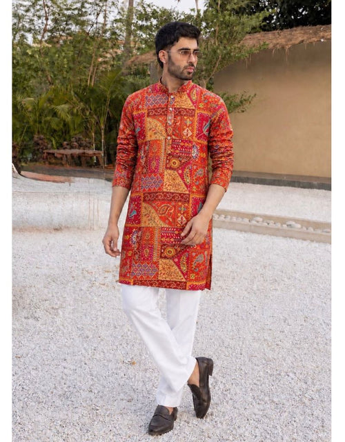 Load image into Gallery viewer, A man wearing a vibrant red and orange patchwork-patterned kurta with white trousers and dark loafers, standing outdoors on a light-colored gravel path.
