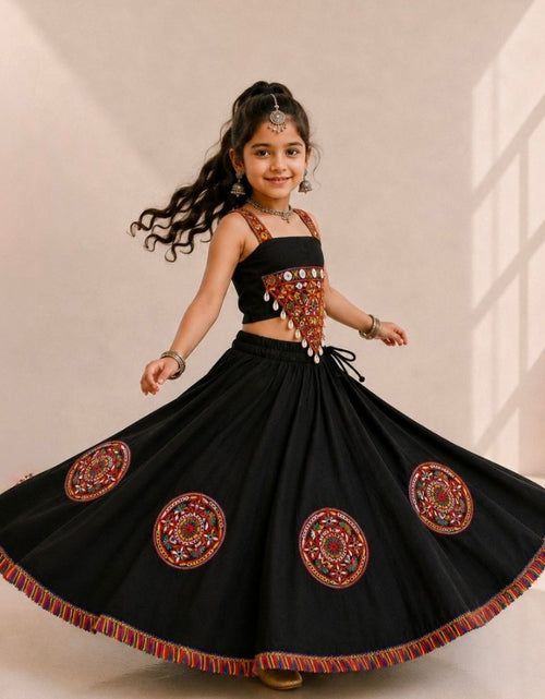 Load image into Gallery viewer, A young girl with long dark hair is wearing a black traditional Indian outfit with ornate red, gold, and silver embroidery, including a sleeveless top and a flared skirt with circular embroidered motifs. She is posing in a studio with a beige background.
