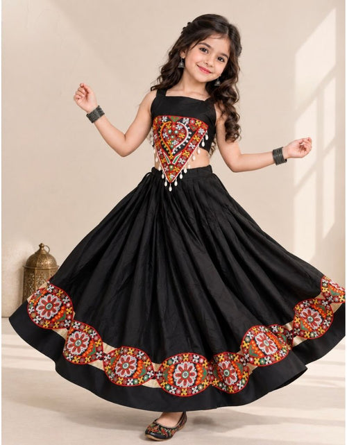 Load image into Gallery viewer, A young girl modeling a black traditional Indian lehenga choli dress with vibrant multicolor floral embroidery on the bodice and flared skirt hem, set against a warm beige background.
