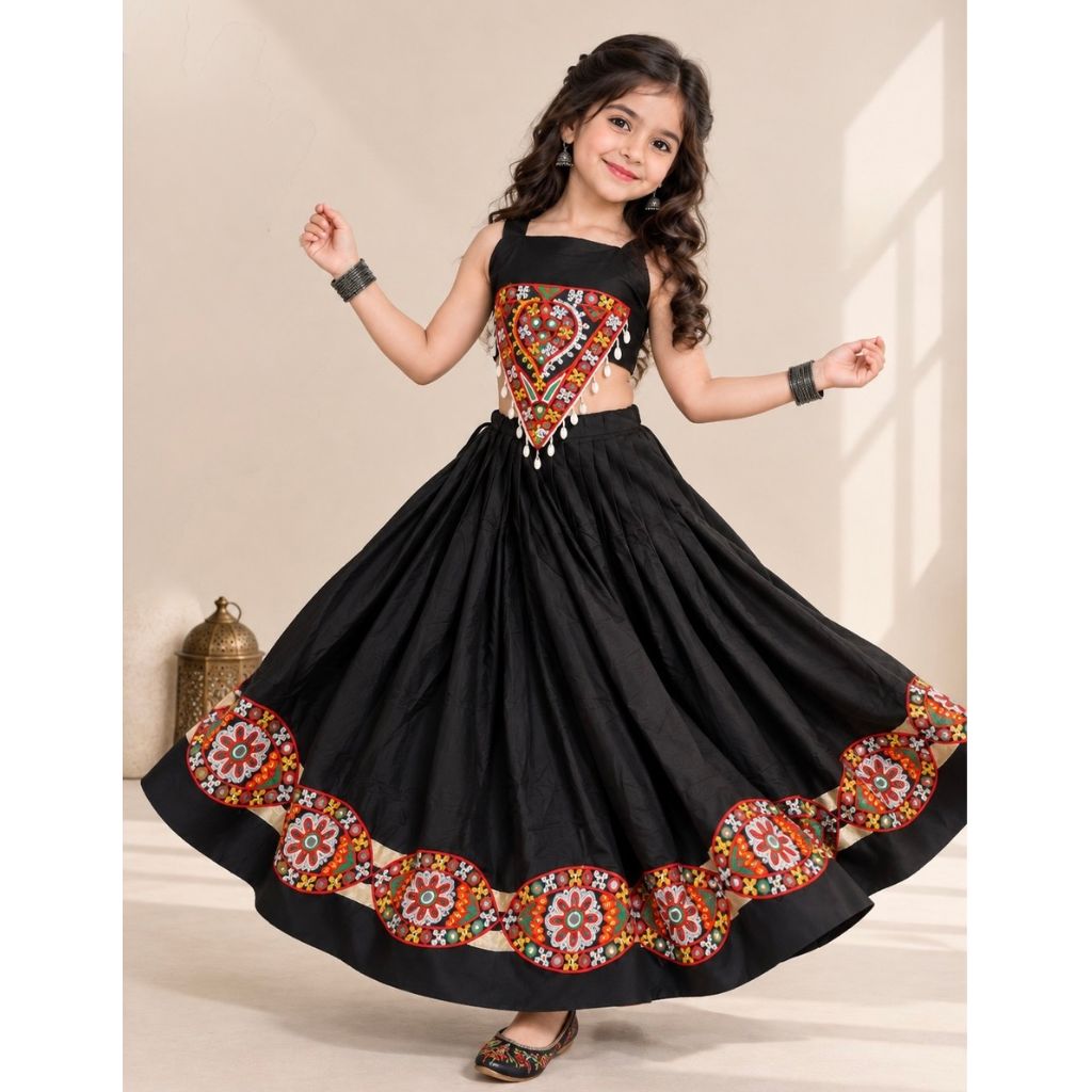 A young girl modeling a black traditional Indian lehenga choli dress with vibrant multicolor floral embroidery on the bodice and flared skirt hem, set against a warm beige background.