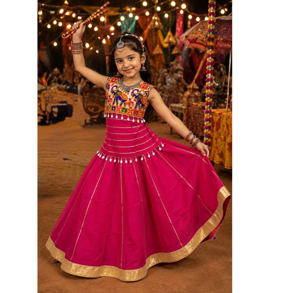 A young girl wearing a bright magenta pink traditional Indian lehenga choli dress with gold borders and colorful embroidered details on the bodice, posing and twirling in a festive indoor setting with string lights and decorations.