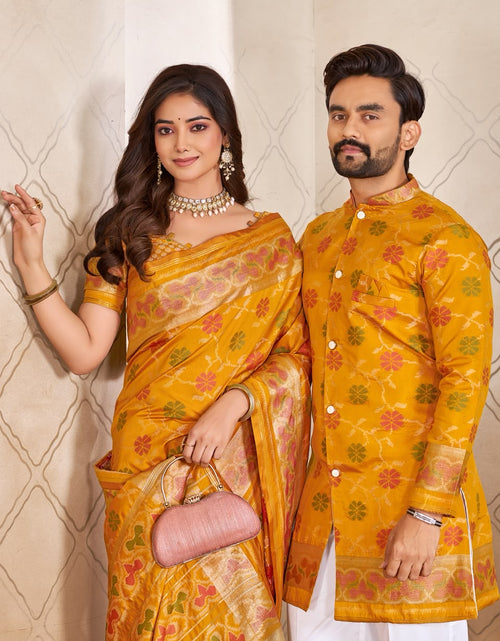 Load image into Gallery viewer, A couple wearing traditional Indian formal wear, featuring a woman in a yellow and gold patterned saree and a man in a matching yellow embroidered kurta, standing against a beige patterned wall.
