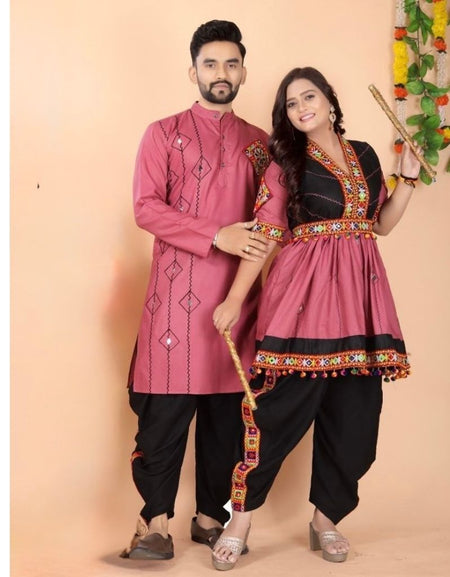 A man and a woman modeling traditional Indian ethnic Navratri couple matching wear. The man wears a dusty pink embroidered kurta with black pants, and the woman wears a matching dusty pink and black kurta with ornate gold and red embroidery, paired with black pants.