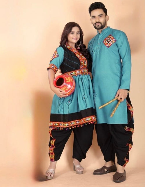 Load image into Gallery viewer, A couple modeling traditional Navratri Matching Outfit clothing against a solid beige studio backdrop. The woman wears a turquoise and black kurta with colorful embroidered borders and black pants, holding a red pot.
