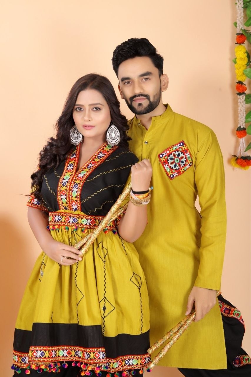 A couple posing in traditional Indian couple wear matching Navratri ethnic wear. The woman wears a yellow and black embroidered kurta and Dhoti set, while the man wears a solid yellow kurta and black dhoti