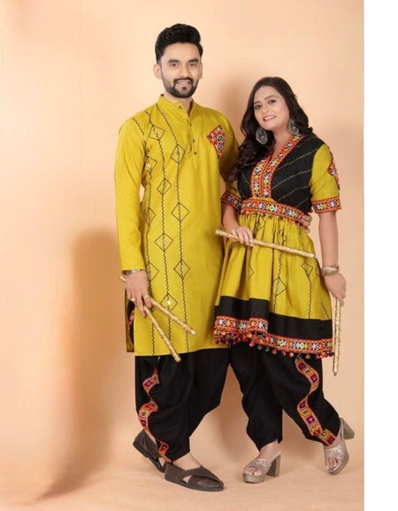 A couple modeling traditional Indian Navratri couple ethnic wear against a solid peach studio backdrop. The man wears a yellow kurta with black pants, and the woman wears a matching yellow and black kurta with red and gold border details.