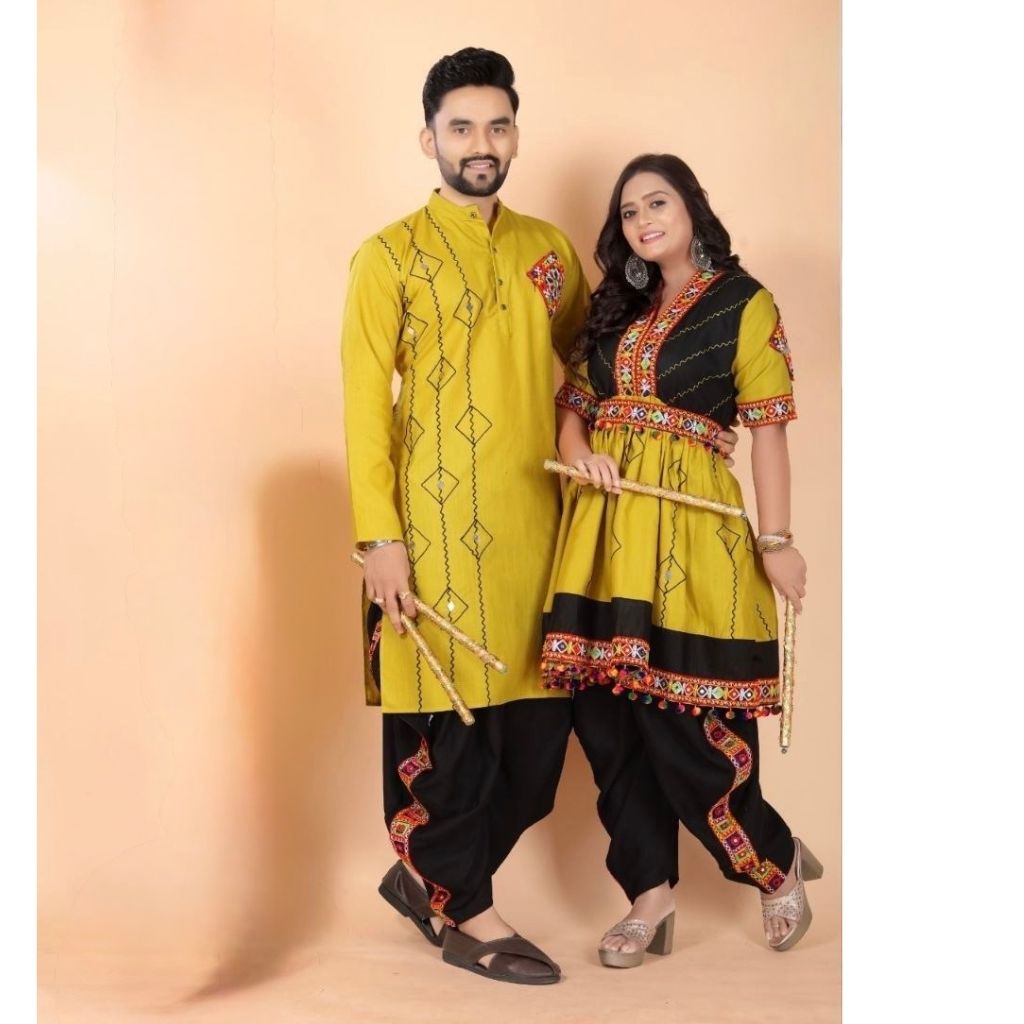 A couple modeling traditional Indian Navratri couple ethnic wear against a solid peach studio backdrop. The man wears a yellow kurta with black pants, and the woman wears a matching yellow and black kurta with red and gold border details.
