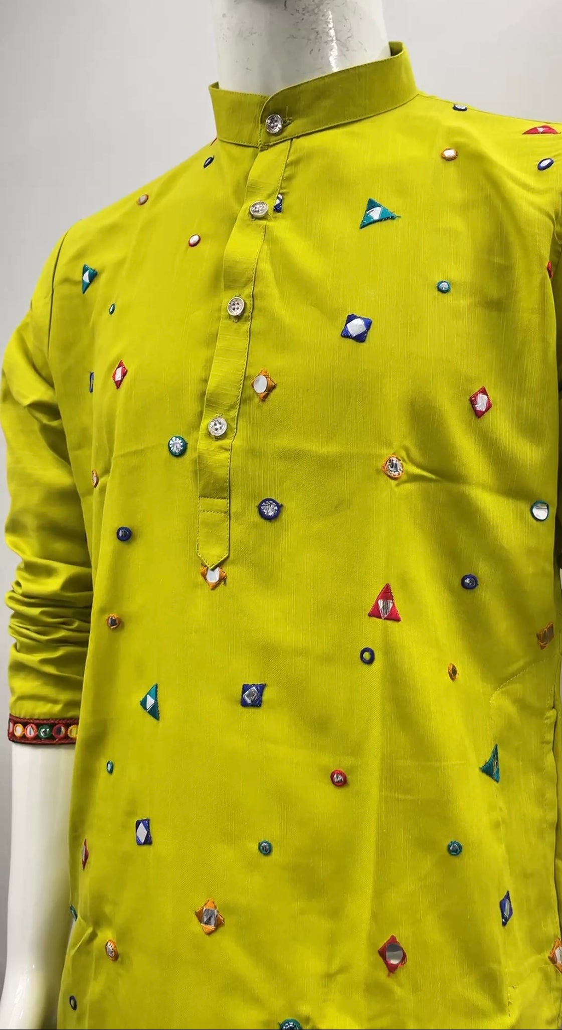 A bright yellow-green kurta displayed on a mannequin, featuring a mandarin collar, buttoned front placket, and scattered colorful embroidered geometric motifs.