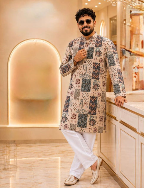 Load image into Gallery viewer, A man wearing a beige long kurta with a multicolor patchwork print and white trousers, standing in a modern, warmly lit interior space.
