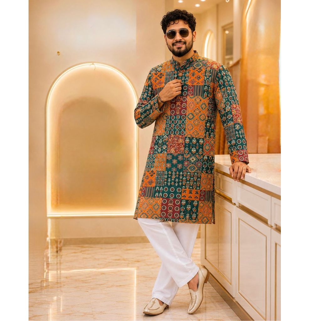 A man wearing a multicolor patchwork-patterned kurta with white trousers and beige shoes, posing in a modern, warmly lit interior setting.