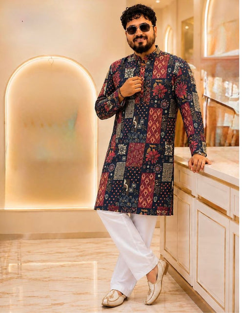 Load image into Gallery viewer, A man wearing a long-sleeved kurta with red and gold patchwork patterns, paired with white trousers and gold shoes, posing in a modern, warm-toned interior setting.
