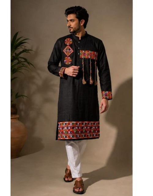 Load image into Gallery viewer, A man modeling a Navratri Festive wear black long kurta with colorful embroidered patterns on the chest, cuffs, and hem, paired with white trousers and brown sandals in a studio setting.
