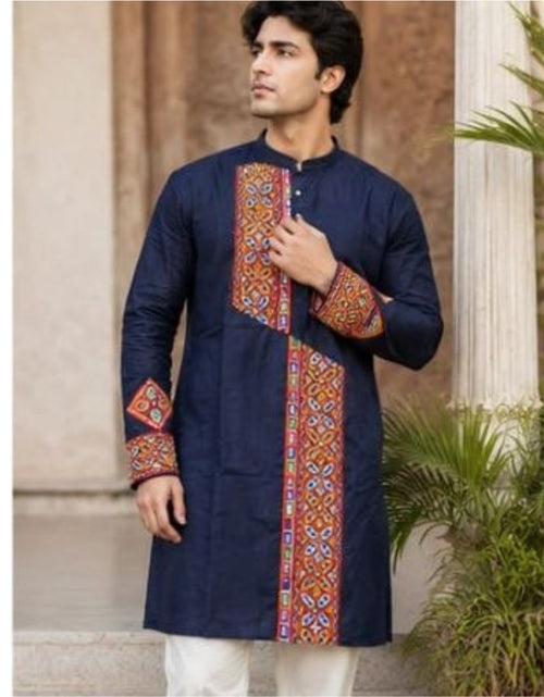Load image into Gallery viewer, A man wearing a navy blue kurta with colorful geometric embroidered panels on the front and cuffs, paired with white trousers, standing outdoors in front of a stone column and plants.
