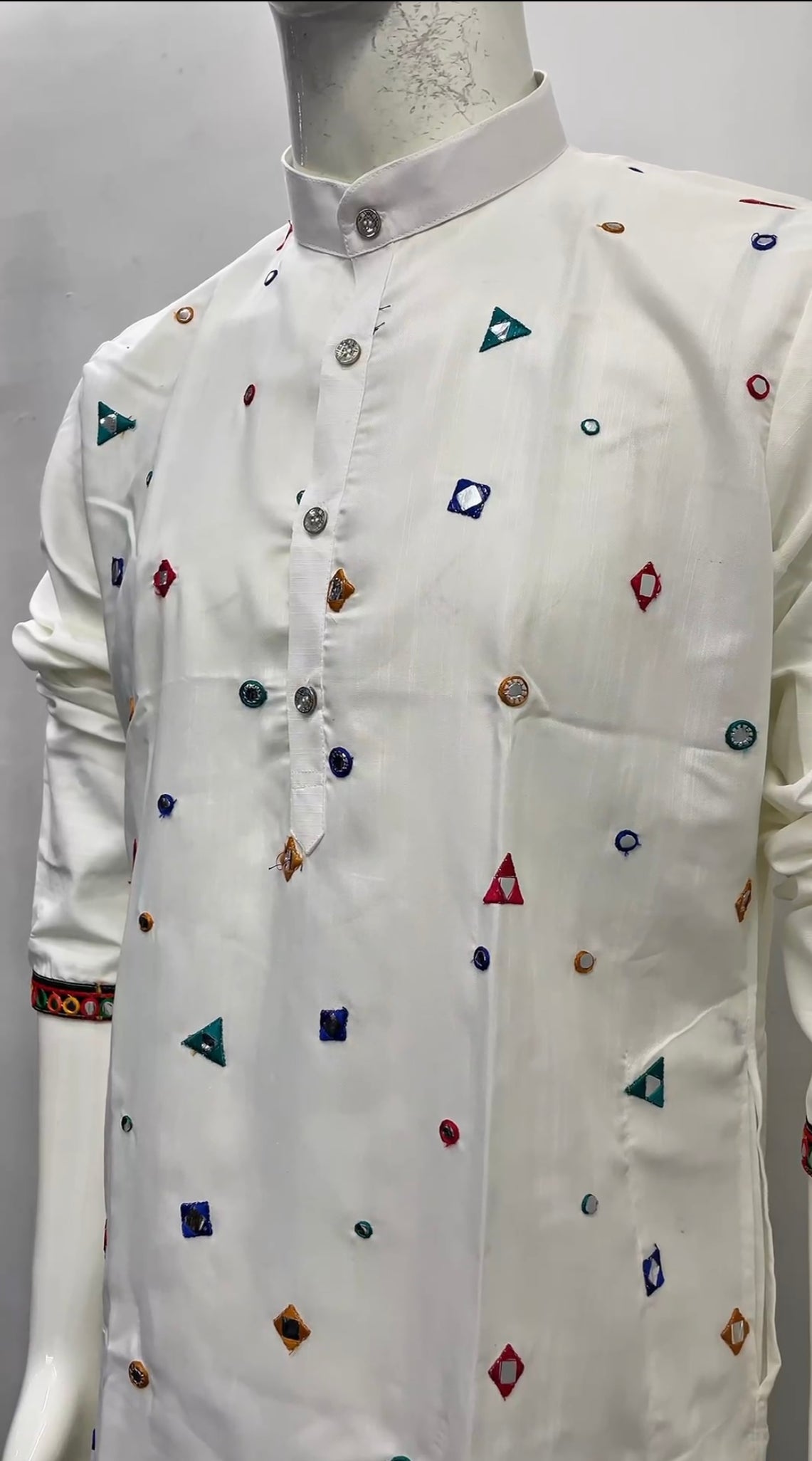 A white long-sleeve kurta with colorful geometric embroidered motifs, displayed on a mannequin torso against a plain light gray background.