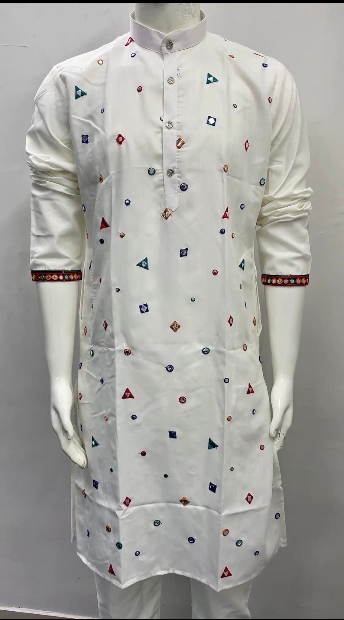 A white long kurta displayed on a mannequin, featuring small multicolored geometric prints and patterned trim on the cuffs.