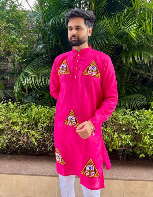 Load image into Gallery viewer, A man wearing a bright pink kurta with embroidered geometric patterns on the chest and lower hem, paired with white trousers, standing outdoors in front of green tropical foliage.
