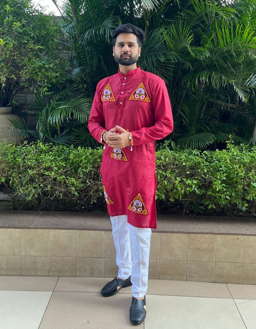 Load image into Gallery viewer, A man wearing a bright red kurta with yellow and white geometric embroidery on the chest and hem, paired with white trousers and black shoes, standing outdoors in front of green plants.
