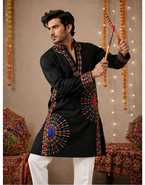 Load image into Gallery viewer, A man wearing a black kurta with colorful embroidered patterns and white pants, holding a decorative staff in a festive indoor setting with hanging marigold garlands and string lights.
