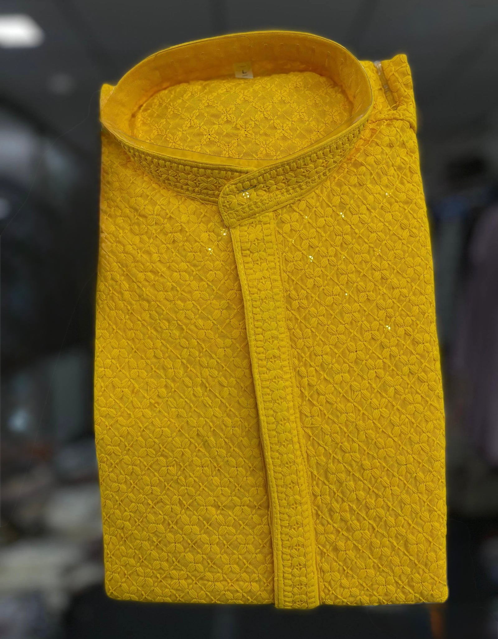 A folded mustard yellow textured shirt with a mandarin collar, displayed against a dark, blurred background.