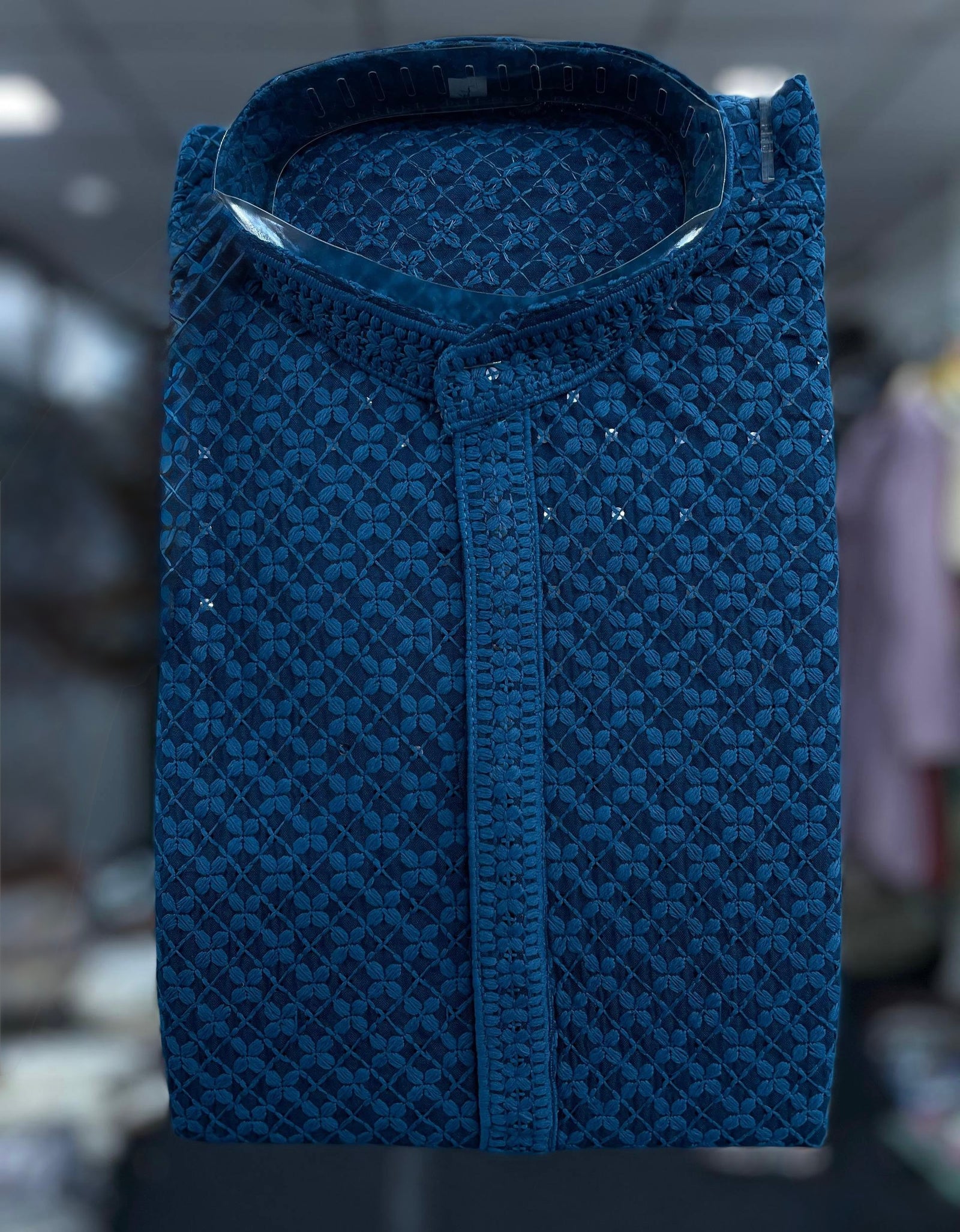 An ethnic blue patterned Kurta with a stand collar and decorative silver embellishments, shown against a blurred indoor background.