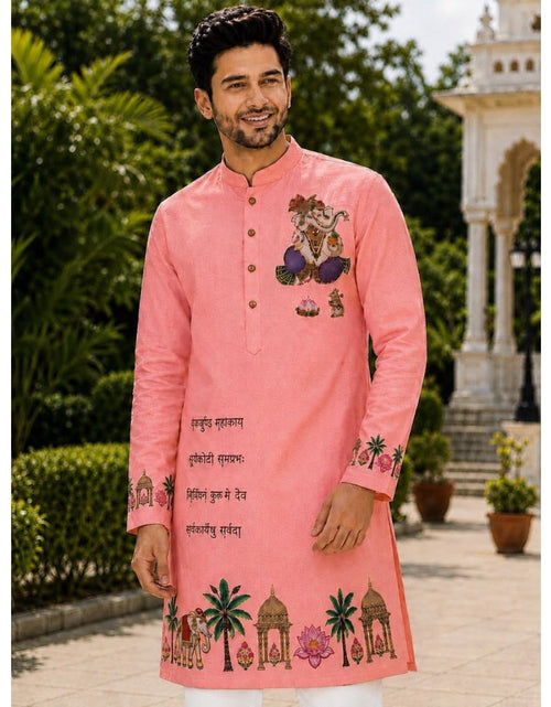 Load image into Gallery viewer, A man wearing a pink Indian kurta with traditional embroidery and text, standing outdoors in front of a garden and architectural background.
