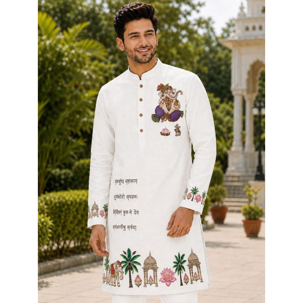 A man wearing a white long-sleeve kurta with colorful traditional Indian embroidery, standing outdoors in front of a garden and a white architectural structure.