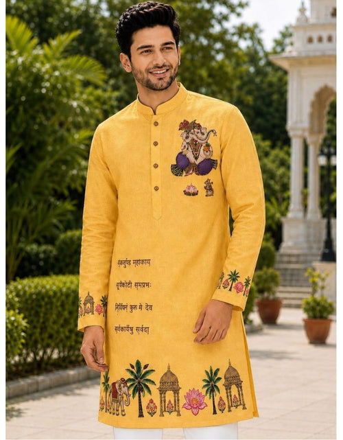 Load image into Gallery viewer, A man wearing a bright yellow Indian kurta with colorful traditional embroidery and text, standing outdoors in a garden setting with a white architectural structure in the background.

