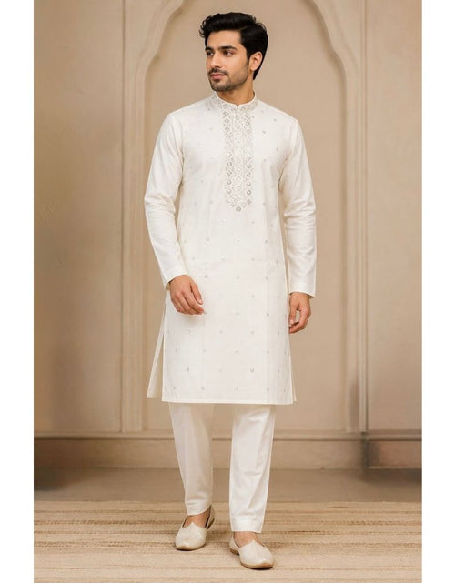 Load image into Gallery viewer, A man wearing a traditional white Indian kurta and matching trousers, standing in front of a beige arched wall background.
