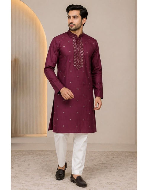 Load image into Gallery viewer, A man modeling a deep maroon long-sleeve kurta with silver embroidery on the chest and scattered motifs, paired with white trousers and black loafers, standing in a studio setting.
