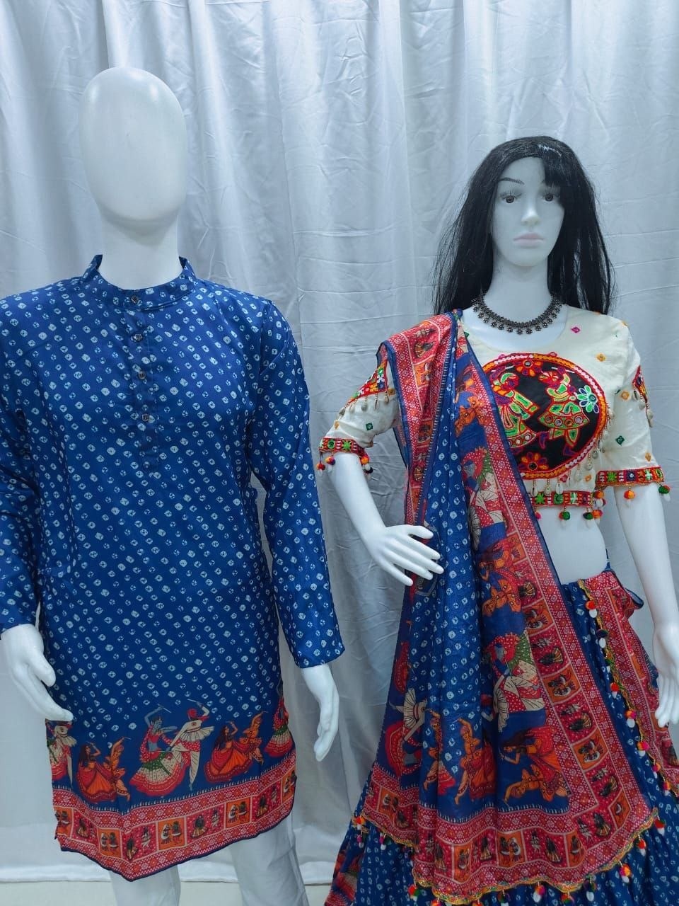 Two mannequins display traditional Indian ethnic wear against a white curtain backdrop. The left mannequin wears a blue kurta with small white motifs and a red border print.