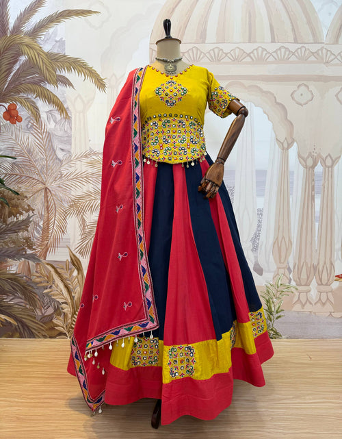Load image into Gallery viewer, A traditional Indian ethnic outfit displayed on a mannequin against a solid gray background. The outfit features a bright yellow embroidered blouse with short sleeves, a flared navy blue skirt with red and yellow border panels, and a red dupatta with colorful geometric borders and white tassels.
