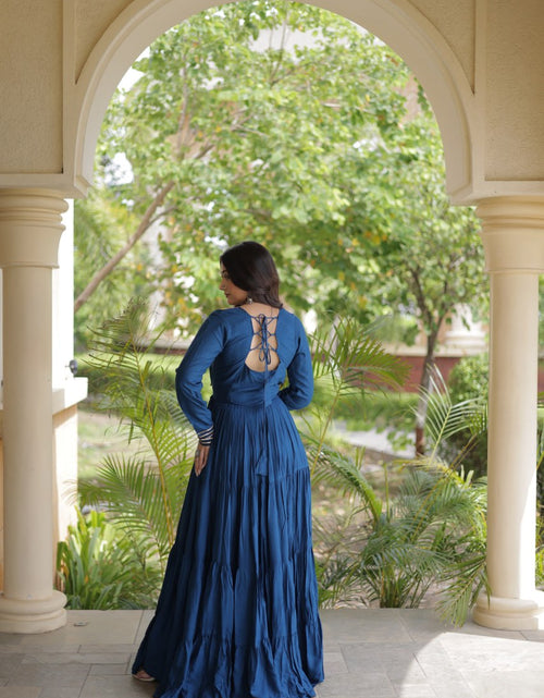 Load image into Gallery viewer, A woman wearing a long-sleeved navy blue maxi dress with an open lace-up back, standing in a stone archway with a lush garden background.
