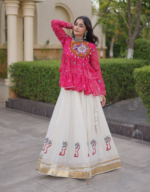 Load image into Gallery viewer, A woman modeling a traditional Indian outfit featuring a bright pink embroidered kurta with a long cream flared skirt decorated with embroidered motifs and a gold border, set against a background of hedges and a building.
