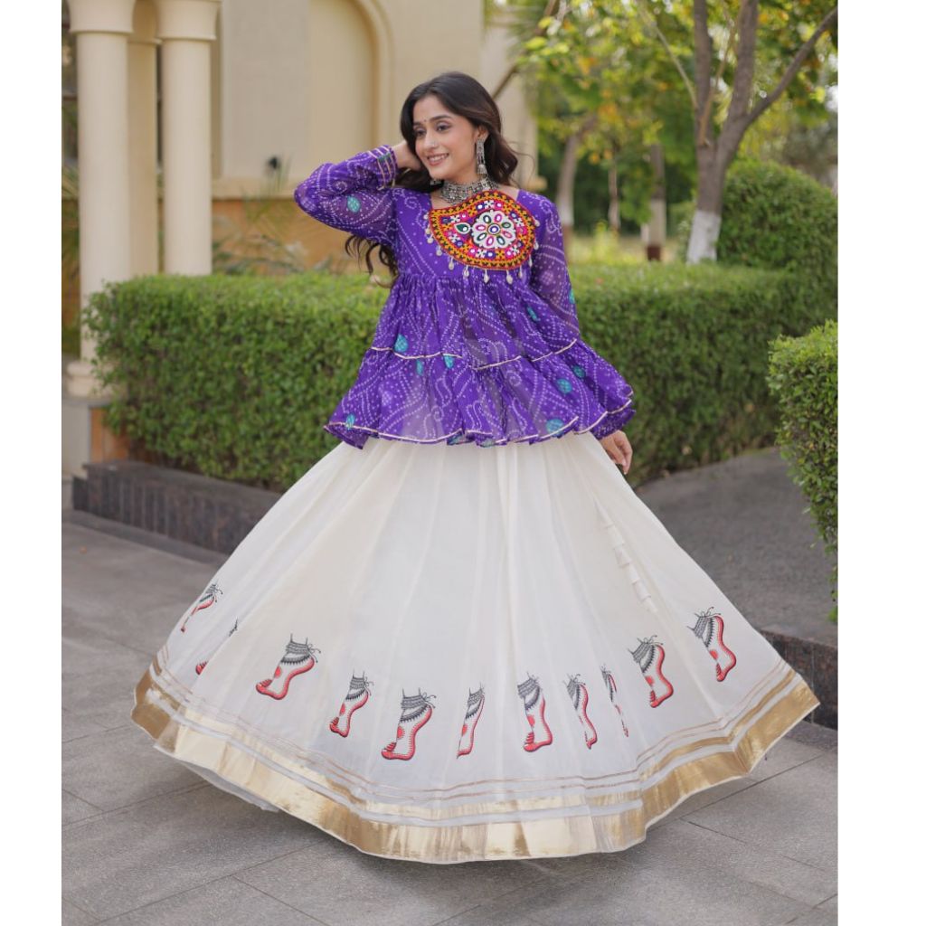 A woman modeling a traditional Indian outfit featuring a purple embroidered kurta paired with a voluminous white nette skirt decorated with red and gray motifs and a gold border, set against a garden background.