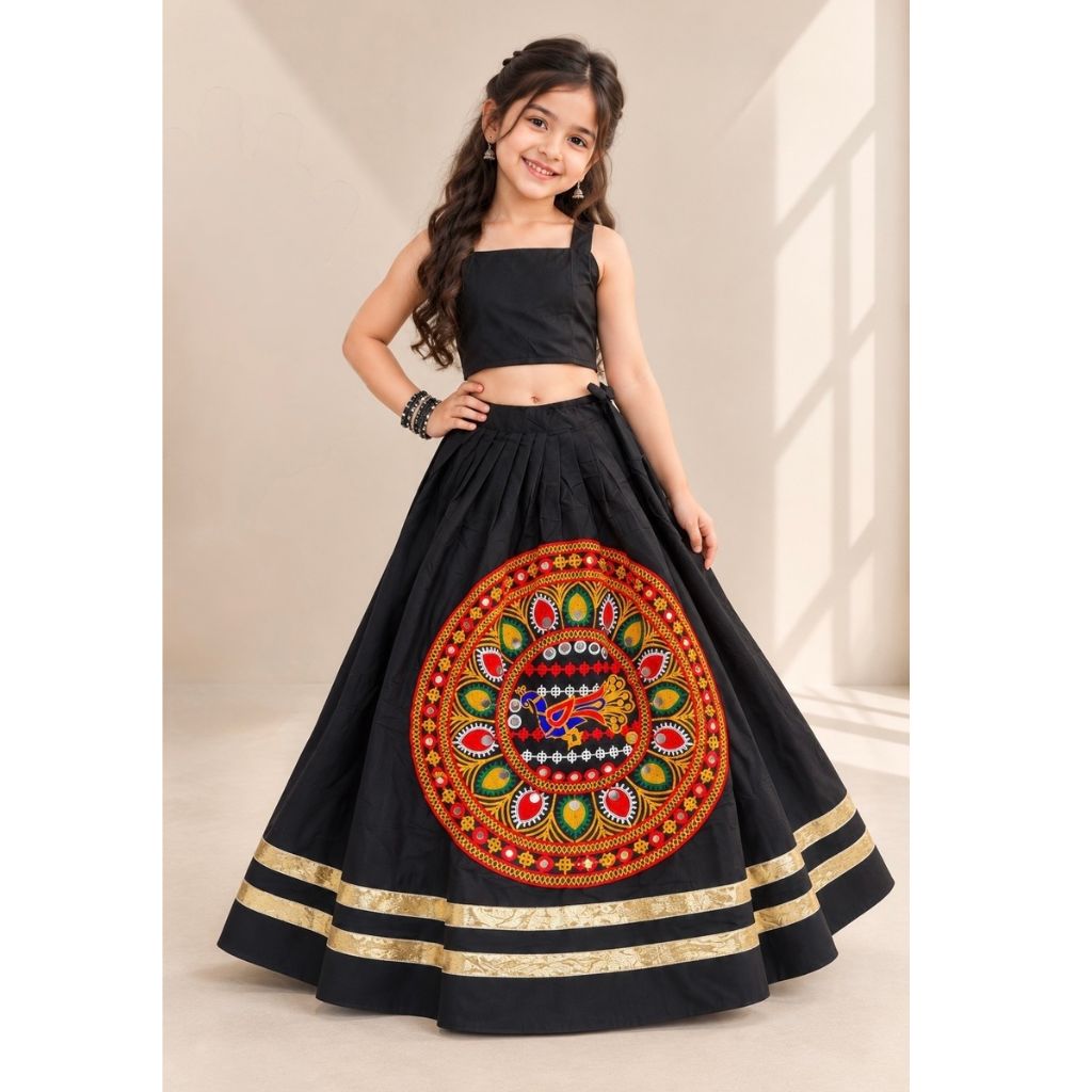 A young girl modeling a black traditional Indian ethnic wear set consisting of a sleeveless crop top and a flared skirt with a large colorful circular embroidered motif on the front and gold stripes near the hem.