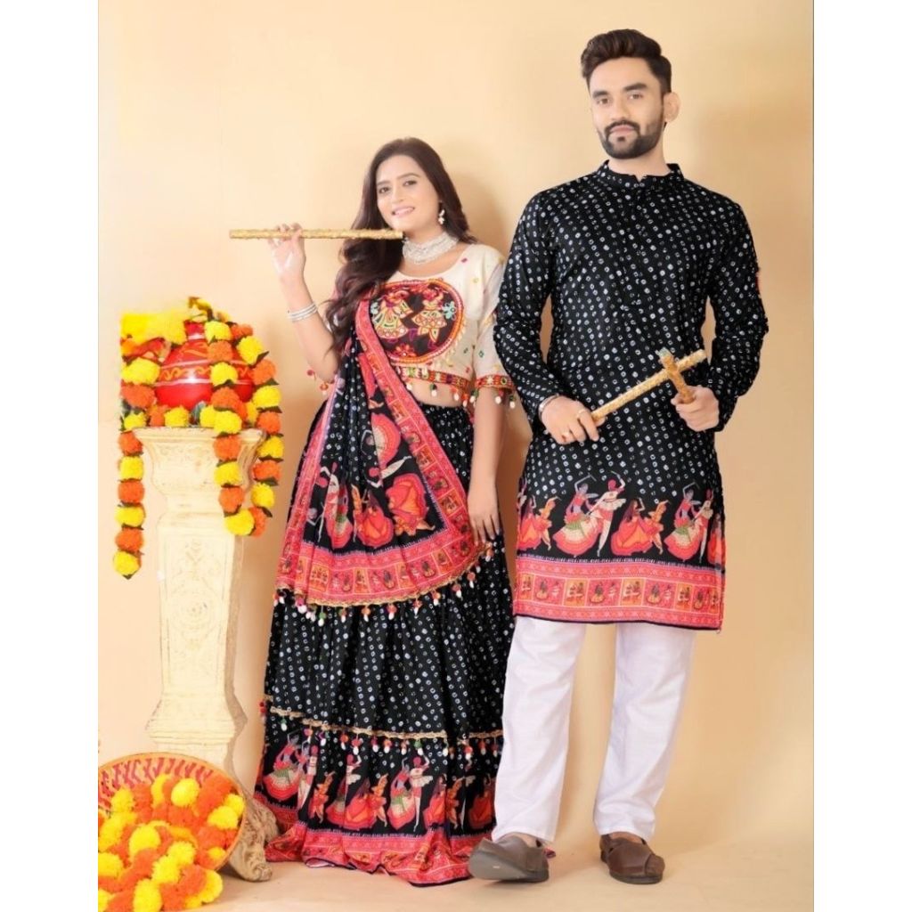 A couple modeling traditional Indian festive clothing. The woman wears a black and red lehenga choli with a white embroidered bodice, while the man wears a matching black kurta with red and gold motifs and white pants.