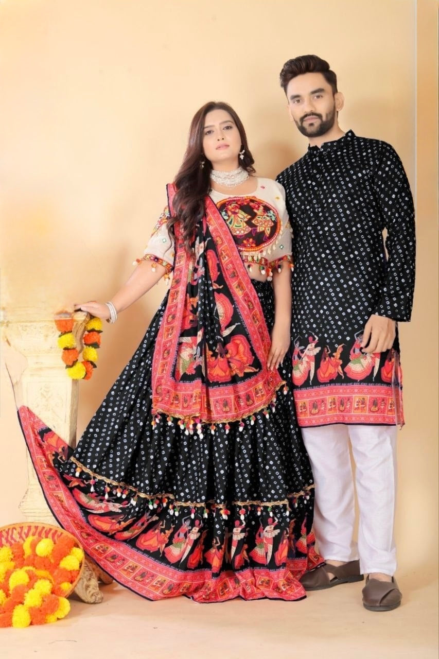A couple posing in traditional Indian Navratri attire. The woman wears a black and red printed lehenga choli with a white blouse, and the man wears a matching black kurta with white pants.