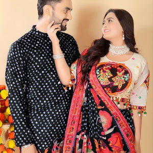A couple wearing traditional South Asian clothing, featuring a black kurta with white polka dots and a matching black salwar with a vibrant red and multicolor embroidered dupatta, set against a plain beige background.