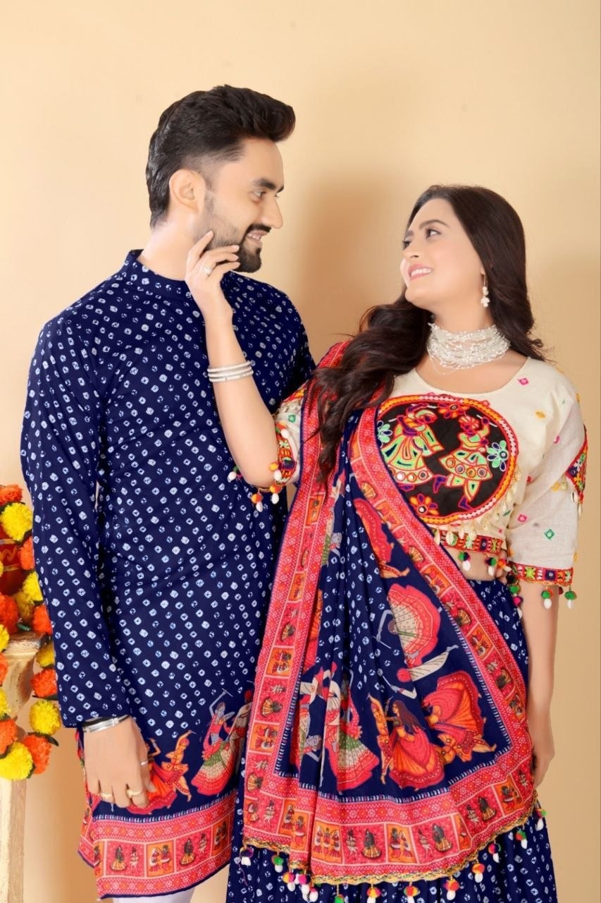 A couple wearing matching traditional South Asian outfits. The man wears a navy blue kurta with small white dots, and the woman wears a matching navy blue and pink dupatta over a cream-colored embroidered kurta.