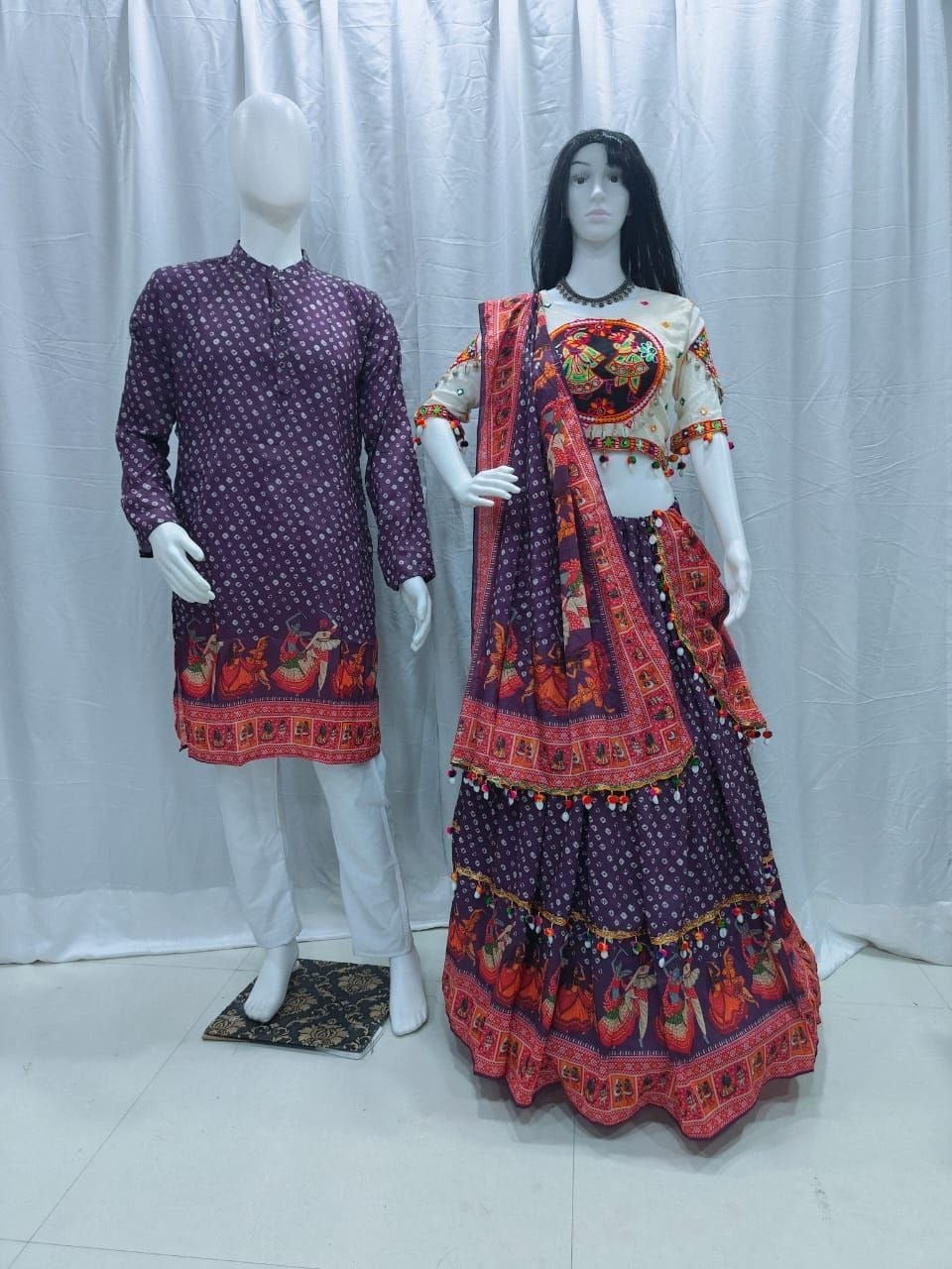 A traditional Indian ethnic wear set displayed on mannequins, featuring a matching men's kurta and women's lehenga choli in deep purple with red and orange patterns.