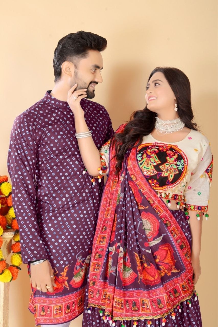 A couple wearing traditional South Asian clothing, featuring a man in a purple patterned kurta and a woman in a matching purple and red printed saree with a cream embroidered blouse, set against a plain beige background.