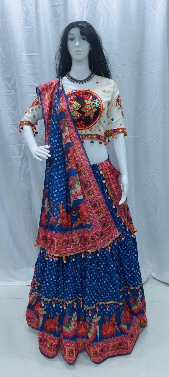 A traditional Indian lehenga choli set displayed on a white mannequin. The set features a deep blue skirt with red and gold border prints, a cream-colored blouse with a large red and gold circular motif on the chest, and a matching blue dupatta with red and gold borders.