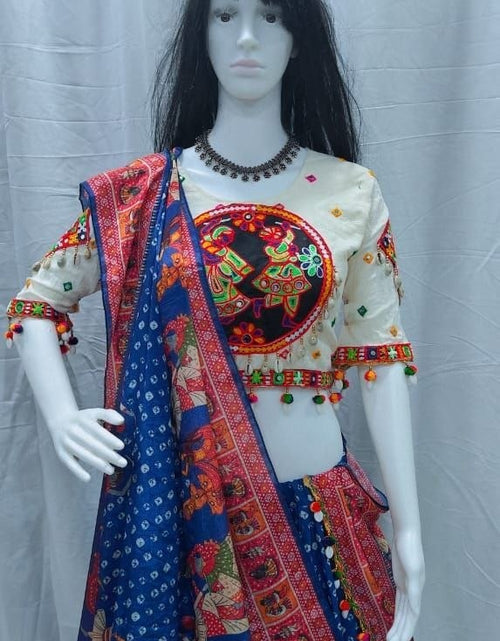 Load image into Gallery viewer, A traditional Indian ethnic wear set displayed on a female mannequin, featuring a blue printed lehenga skirt, a cream-colored embroidered blouse with colorful details, and a matching blue dupatta with red and gold patterns.
