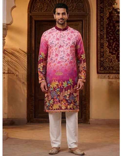 Load image into Gallery viewer, A man modeling a vibrant pink and magenta printed traditional Indian kurta with colorful floral and scenic motifs, paired with white trousers and beige shoes, standing in front of an ornate wooden door.
