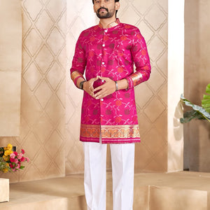 A man modeling a bright pink Indian ethnic kurta with gold and silver embroidery, paired with white trousers and brown sandals, standing on beige stone steps.